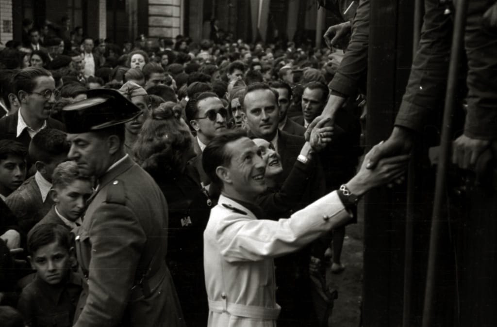 Dionisio Ridruejo,  rodeado por una multitud,   estrecha la mano de  varios hombres subidos en un tren