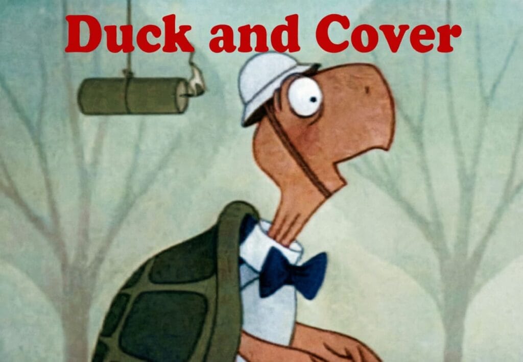 Bert la tortuga animada con casco y pajarita mira con sorpresa un cartucho de dinamita encendido bajo el texto rojo Duck and Cover.