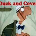 Bert la tortuga animada con casco y pajarita mira con sorpresa un cartucho de dinamita encendido bajo el texto rojo Duck and Cover.