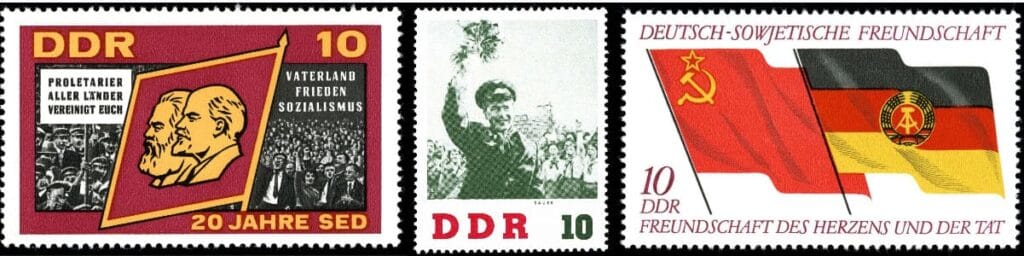 Tres sellos postales de la RDA con iconografia de Marx y Lenin, desfiles populares y banderas de la hermandad aleman-sovietica.