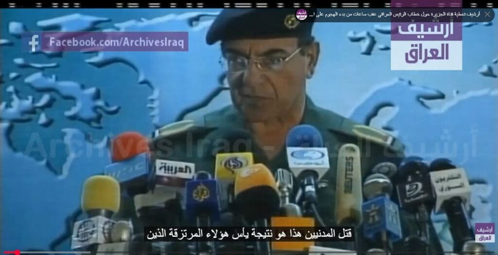 Mohamed Said al-Sahaf habla ante una multitud de micrófonos con un mapa del mundo difuminado de fondo en una emisión de televisión.