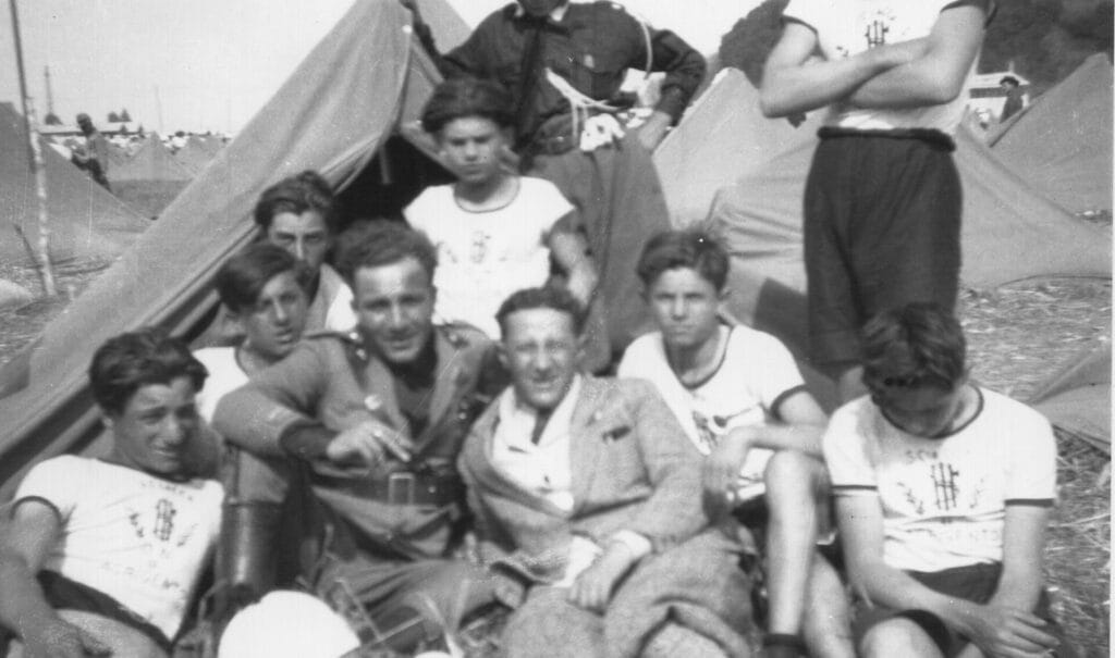 Grupo de adolescentes y jóvenes italianos posando frente a tiendas de campaña militares durante un campamento de adoctrinamiento estatal.
