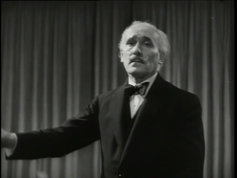 Arturo Toscanini con esmoquin dirigiendo una orquesta en un fotograma en blanco y negro del documental Hymn of the Nations de 1944.