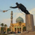 Pintura al óleo que recrea el derribo de la estatua de Sadam Husein mediante grúas en la plaza Firdos de Bagdad con mezquita detrás.