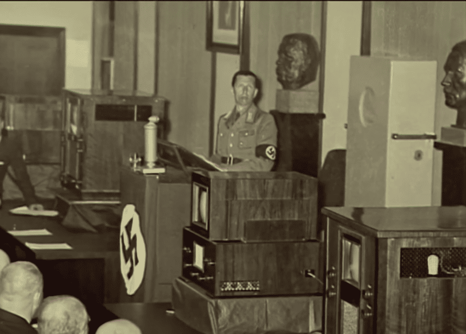 Eugen Hadamovsky pronuncia un discurso ante micrófonos y monitores con simbología nazi en la estación de televisión Fernsehsender Paul Nipkow.