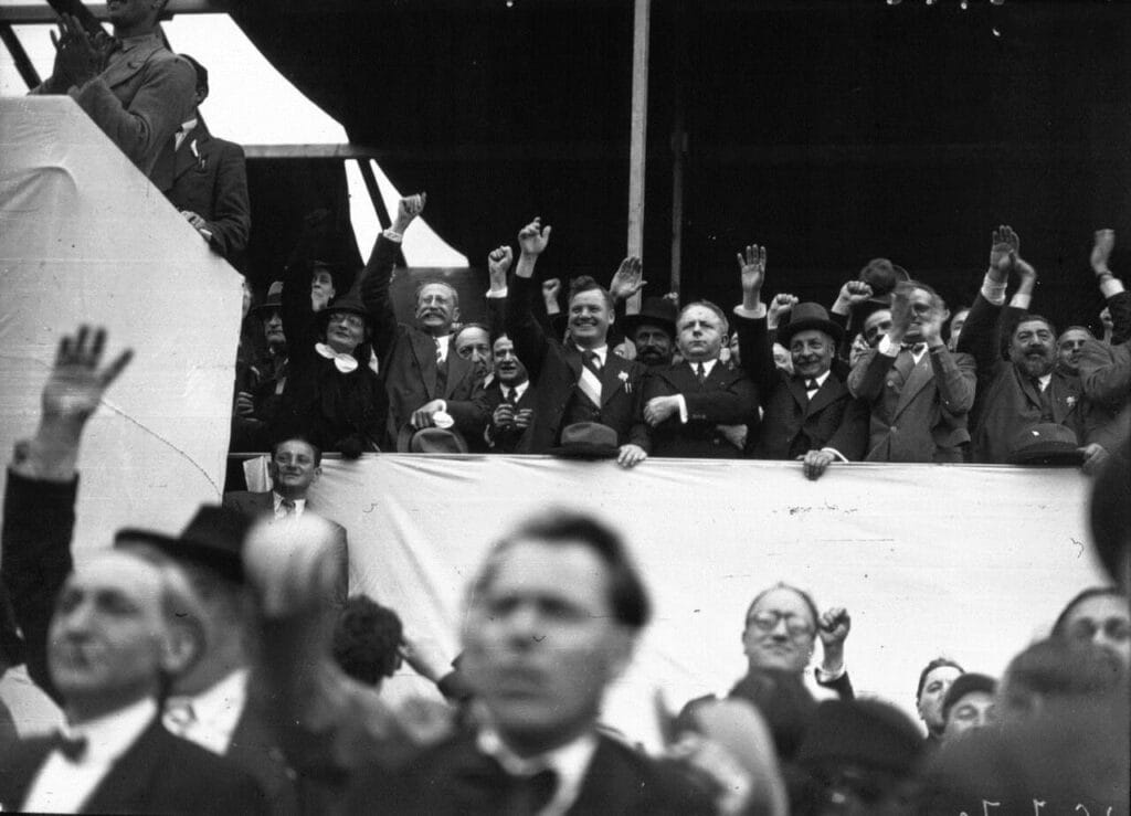 Políticos y asistentes puño en alto cantando La Internacional en tribuna del Front Populaire en Francia, 1936.