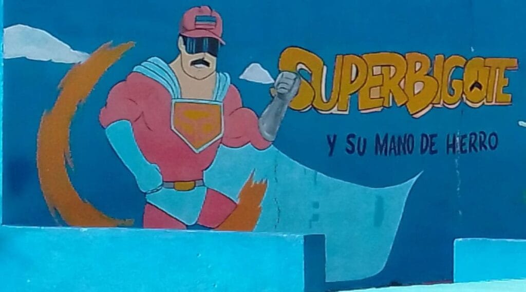 Mural pintado en una pared azul con el personaje Súper Bigote y el texto Y su mano de hierro.