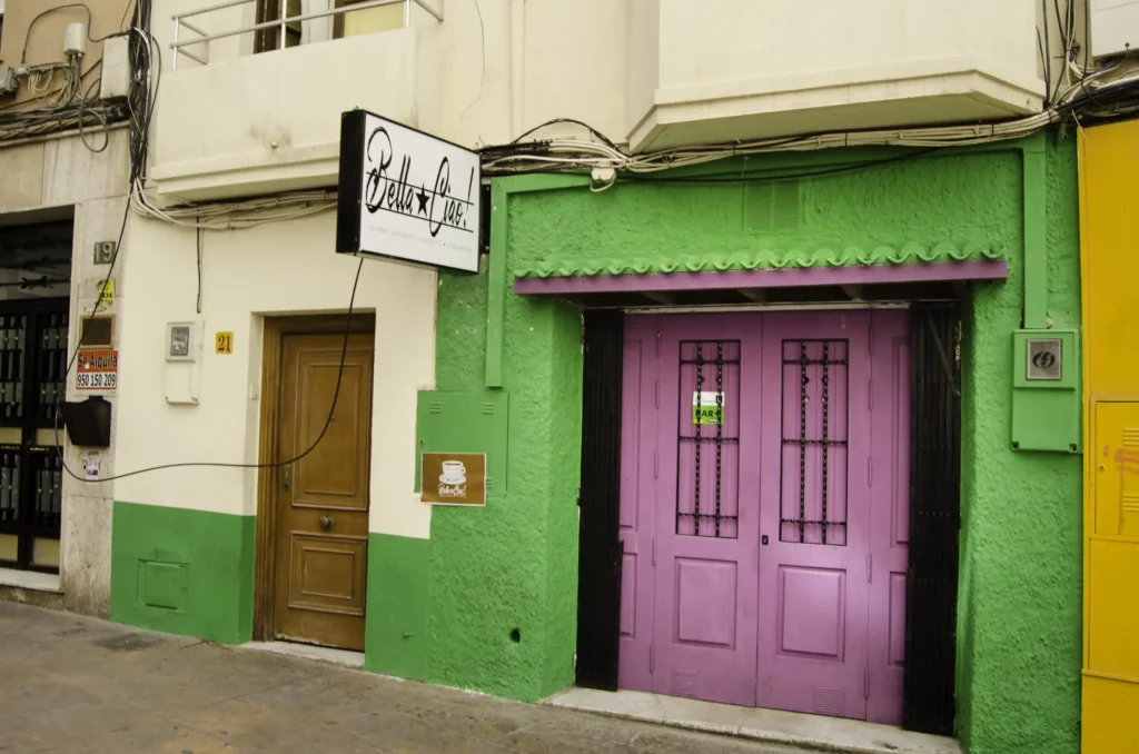 Fachada de la taberna Bella Ciao con paredes verdes, puertas violetas y rótulo negro que dice Under Workers Control sobre la entrada.