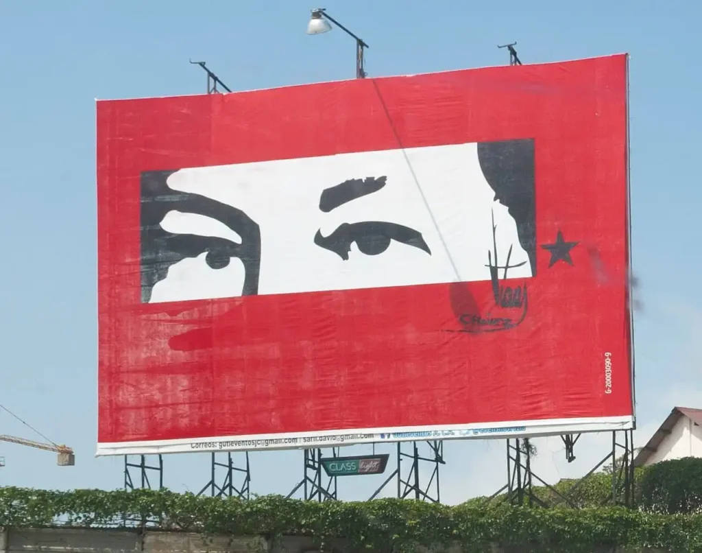 Valla publicitaria de propaganda chavista roja con la icónica mirada estilizada de Hugo Chávez, su firma y una estrella negra.