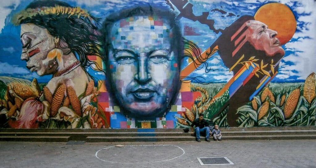 Mural de propaganda chavista con el rostro de Hugo Chávez al centro entre figuras indígenas y maizales.