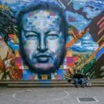 Mural de propaganda chavista con el rostro de Hugo Chávez al centro entre figuras indígenas y maizales.